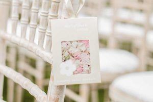 White wooden chairs with padded seats and rail backs and a sachet of flower petals hanging from the back left. 