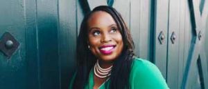 Young Black woman in teal in front of large blue doors. 